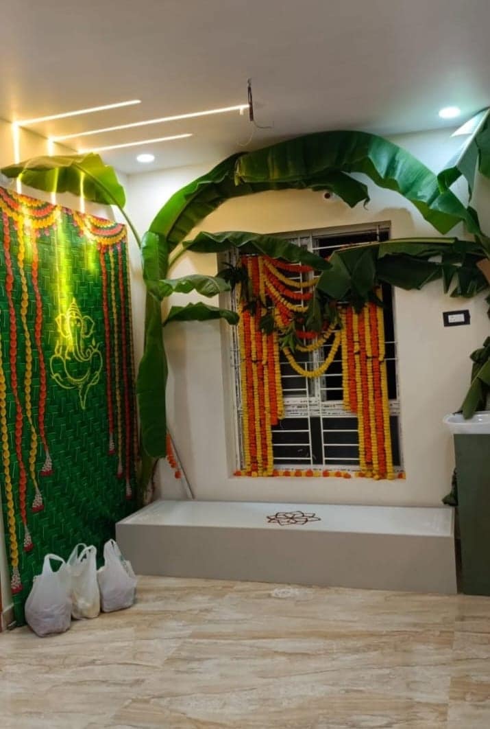 A finished Visakhapatnam home on griha pravesh day, with profile lighting in the ceiling, banana leaves and marigold garlands at the entrance